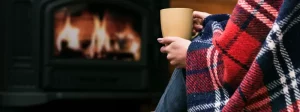 a woman hold a coffee in a blanket next to the fire